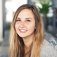 A woman with blonde long hair is smiling, the background is slightly blurred.