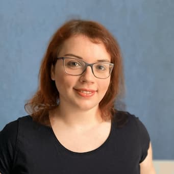 A woman with brown-red shoulder-length hair, glasses and a black shirt looking into the camera. 